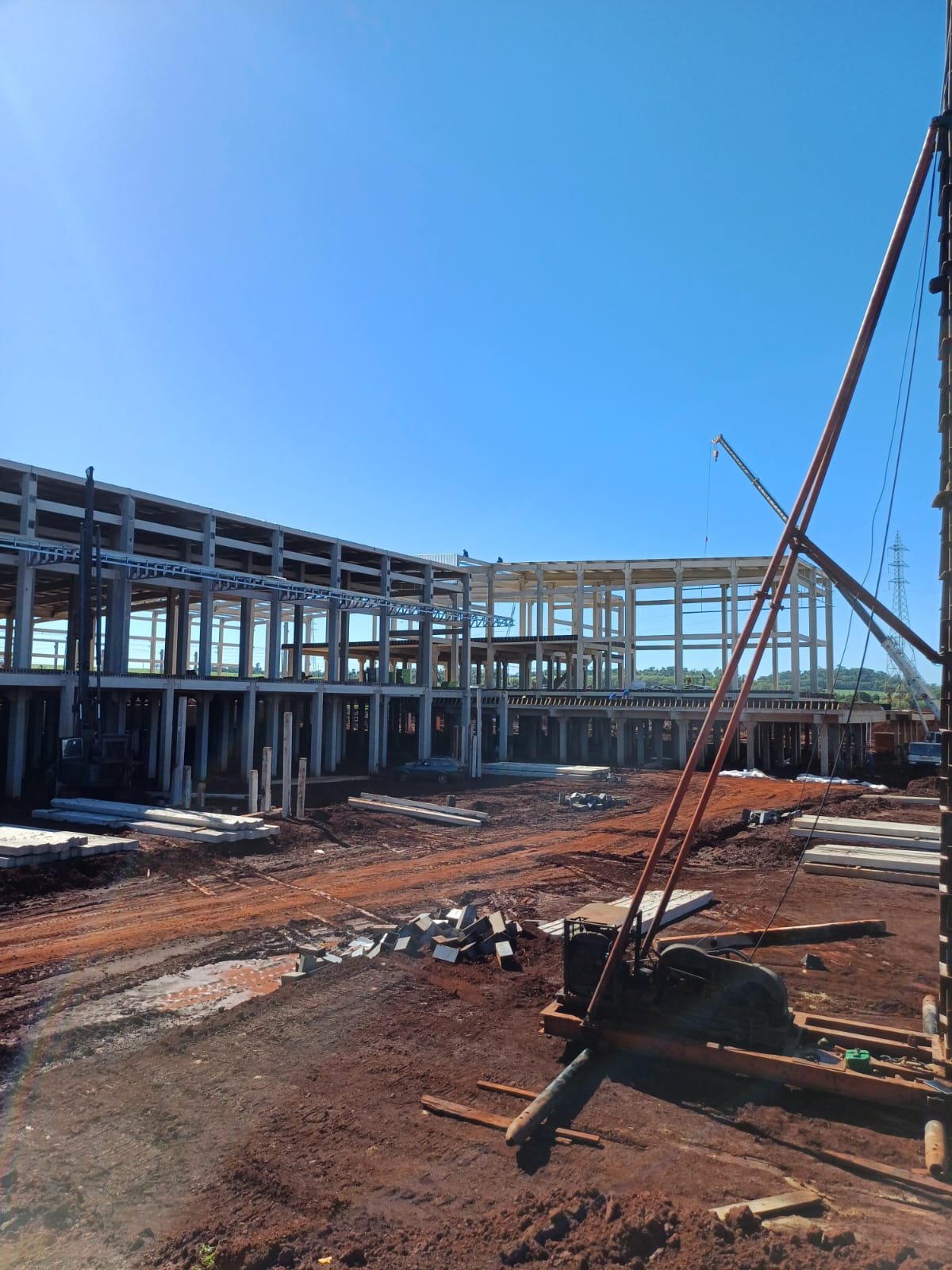 Profissional da Proffunda caminhando em canteiro de obra com grande estrutura pré-moldada ao fundo